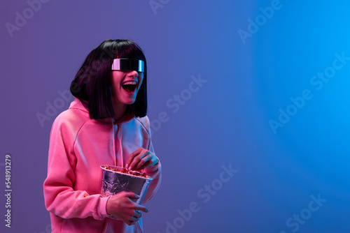 Принти на полотні Laughing excited awesome brunet woman in pink hoodie trendy specular sunglasses eat popcorn look aside posing isolated in blue violet color light background