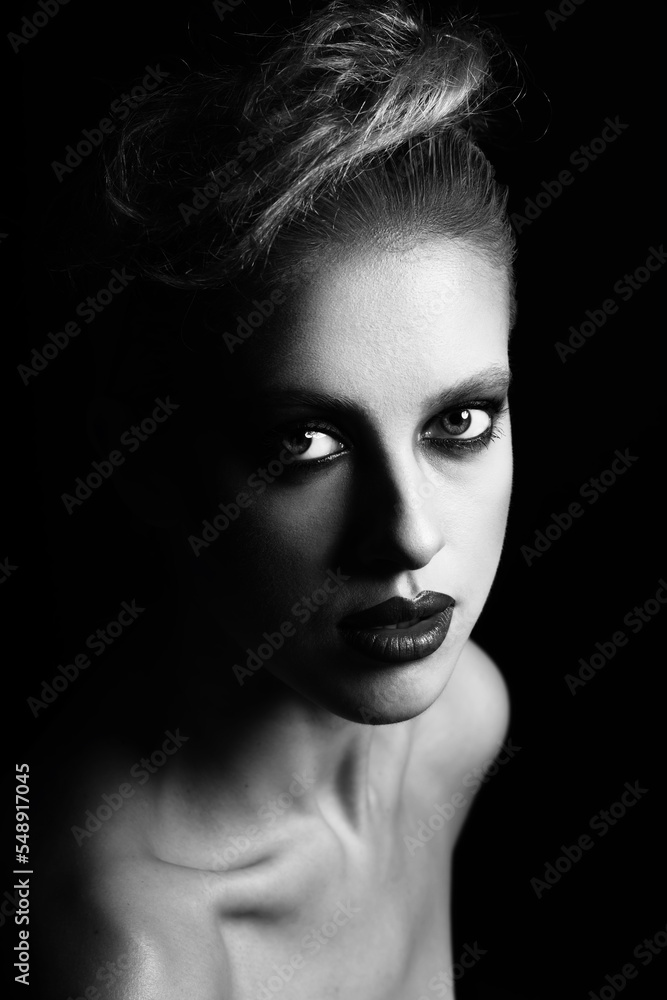 Make-up, hairstyle and fashion concept. Studio portrait of beautiful woman with fancy make-up and lipstick. Model looking at camera with seductive look in dark studio background. Black and white image Make-up, hairstyle and fashion concept. Studio portrait of beautiful woman with fancy make-up and lipstick. Model looking at camera with seductive look in dark studio background. Black and white image
