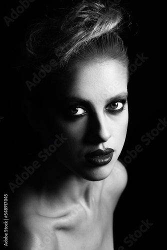 Make-up, hairstyle and fashion concept. Studio portrait of beautiful woman with fancy make-up and lipstick. Model looking at camera with seductive look in dark studio background. Black and white image