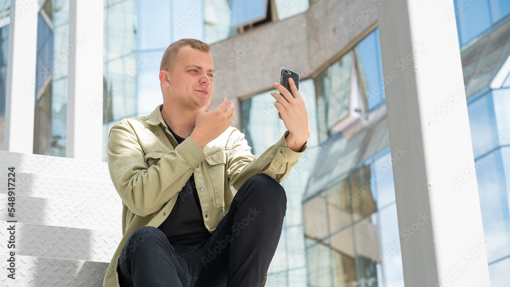 Young man sitting on the stairs and talking sign language via video link on smartphone outdoors. Young man sitting on the stairs and talking sign language via video link on smartphone outdoors.