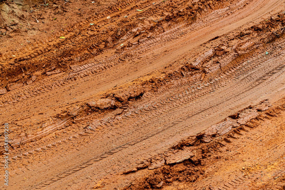 Tire tracks from the wheels of passing cars in the wet, softened ground on a muddy rural road. Mult layers of tire tracks print on dirty red soil. Wheel marks of cars and trucks on countryside route. Tire tracks from the wheels of passing cars in the wet, softened ground on a muddy rural road. Mult layers of tire tracks print on dirty red soil. Wheel marks of cars and trucks on countryside route.