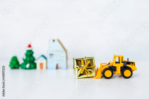 Yellow truck with Christmas gift over blurred house model and tree with space on white background, Festive season concept background, giving gift concept
