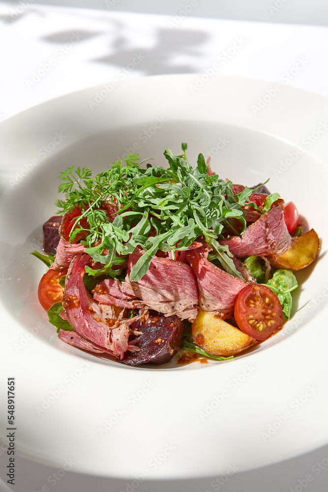 Meat salad with pastrami, baked vegetables and arugula on white background with hard shadows. Salat with roasted beef and vegetables on summer lunch with shadows of leaves. Meat salad with pastrami, baked vegetables and arugula on white background with hard shadows. Salat with roasted beef and vegetables on summer lunch with shadows of leaves.
