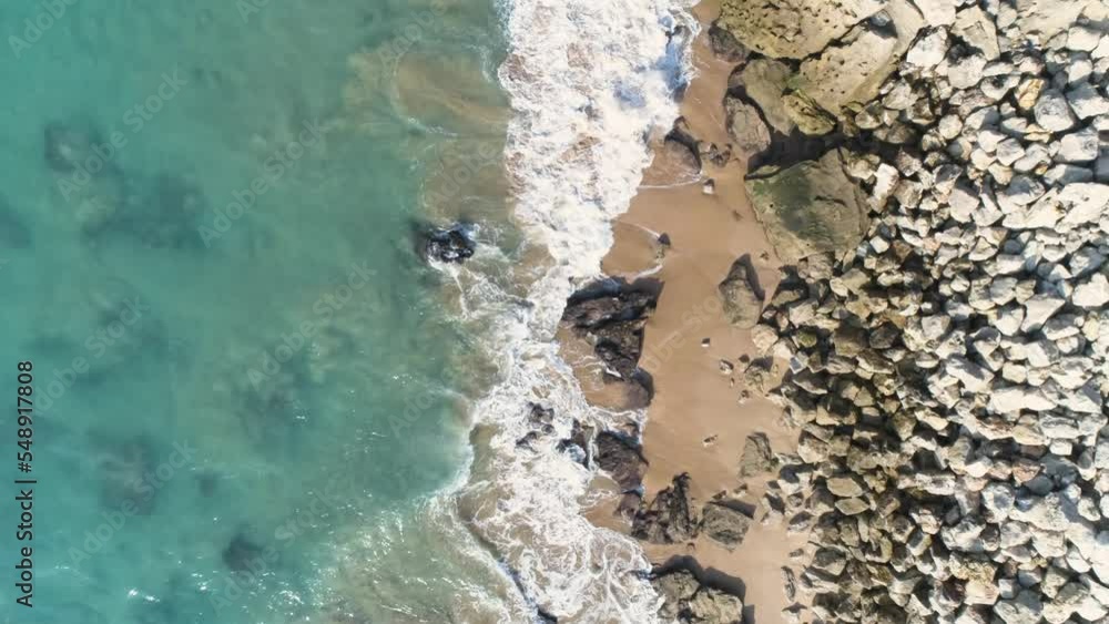 Aerial view of turquoise blue sea waves crashing on rocks and sand on a beautiful sunny day Aerial view of turquoise blue sea waves crashing on rocks and sand on a beautiful sunny day