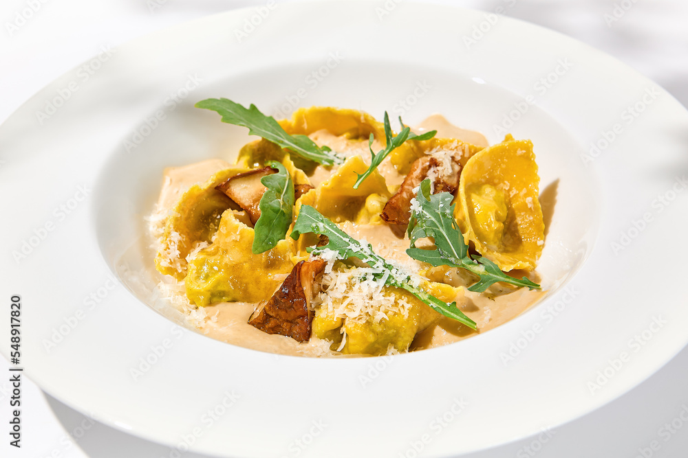 Italian ravioli with meat and mushroom sauce on white plate. Meat tortellini with creamy sauce in summer menu with shadows of tree leaves Ravioli stuffed beef in elegant style Italian ravioli with meat and mushroom sauce on white plate. Meat tortellini with creamy sauce in summer menu with shadows of tree leaves Ravioli stuffed beef in elegant style