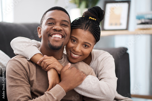 Love, hug and portrait of a happy couple on sofa in the living room of their modern home. Happiness, smile and black woman relax with husband, care and marriage on couch at the house lounge together
