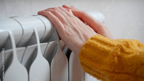 Female hands are trying to keep warm on an aluminum radiator. A woman warms herself near a radiator in winter during the energy crisis in Europe photo