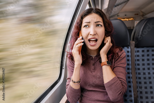 Cuadro en lienzo Annoyed girl is traveling on a train and because of the noise and a bad signal, she cannot hear the interlocutor