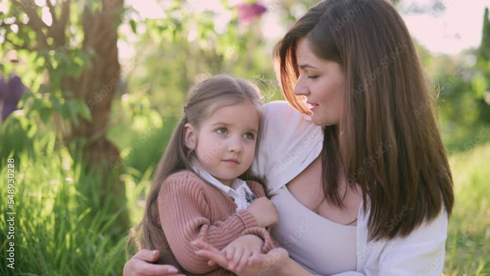 A young mother holds a cute little daughter in her arms near a flowering tree. Portrait of a four-year-old girl in the arms of a loving mother. A young mother holds a cute little daughter in her arms near a flowering tree. Portrait of a four-year-old girl in the arms of a loving mother.