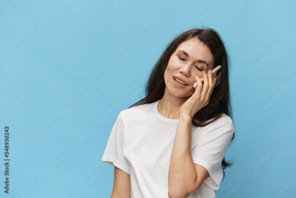woman talking on the phone pleasantly closing her eyes and smiling broadly while standing on a light blue background with empty space to insert an advertising layout woman talking on the phone pleasantly closing her eyes and smiling broadly while standing on a light blue background with empty space to insert an advertising layout