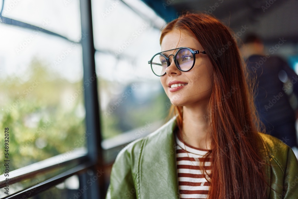 Portrait of a woman with red hair with glasses sitting in a cafe in the city by the window smile with teeth, female freelance blogger close-up Portrait of a woman with red hair with glasses sitting in a cafe in the city by the window smile with teeth, female freelance blogger close-up