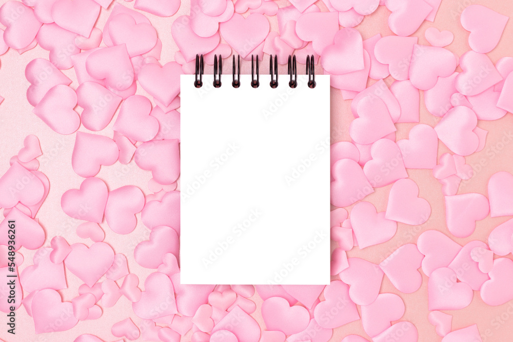 Blank notepad mockup and textile hearts confetti on a pink glittering background. Festive monochrome concept.