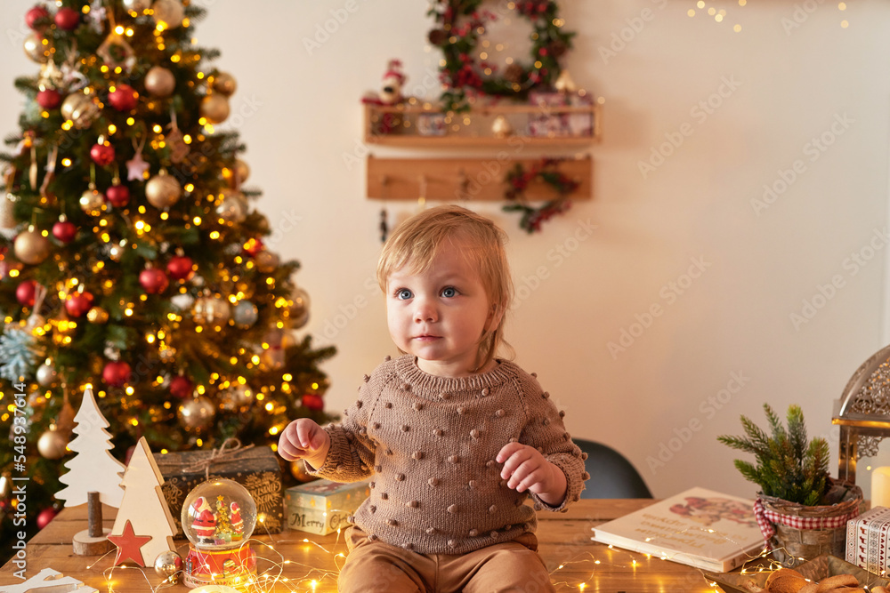 Santa baby. Christmas tree background. Happy New Year! Child in knitted suit