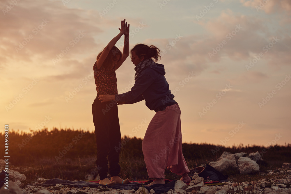 Mother and daughter practicing yoga together in sunset sunrise time in nature.