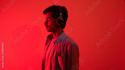 Young man listening to music isolated over red background, chilling and enjoying music, headphones music concept