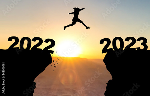 Fotografiet Woman jumps over abyss with sunset in background and inscription 2022 and 2023