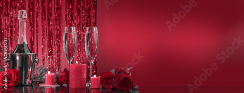 фотографія Bottle in ice bucket and beautiful glasses with sparkling wine, luxurious roses on a mirror surface in a red shining bokeh background