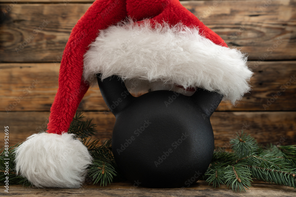 Heavy kettlebell in red Santa Claus hat. Exercise equipment as