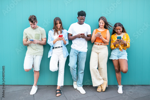 Group multiracial friends using smartphones outside. Group of fashion friends watching on their smart mobile phones. Millennial generation z addicted to new technology trends. 