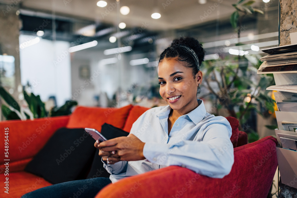 Fototapeta premium Portrait of a businesswoman sitting on the couch, holding a phone.