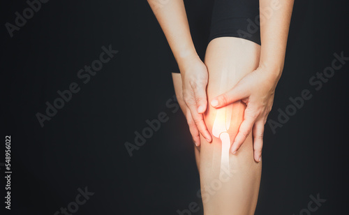 Fototapeta Naklejka Na Ścianę i Meble -  Health concept, person with knee pain, woman holding her knee with a virtual bone image on black  background