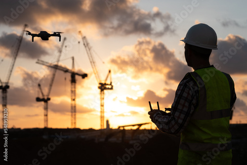 Man launches a quadcopter. An engineer flies a drone next to a construction site. Concept - construction observation with a drone.  Construction cranes on sunset sky 
