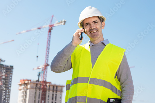 Professional builder standing talking on a phone in front of the construction site