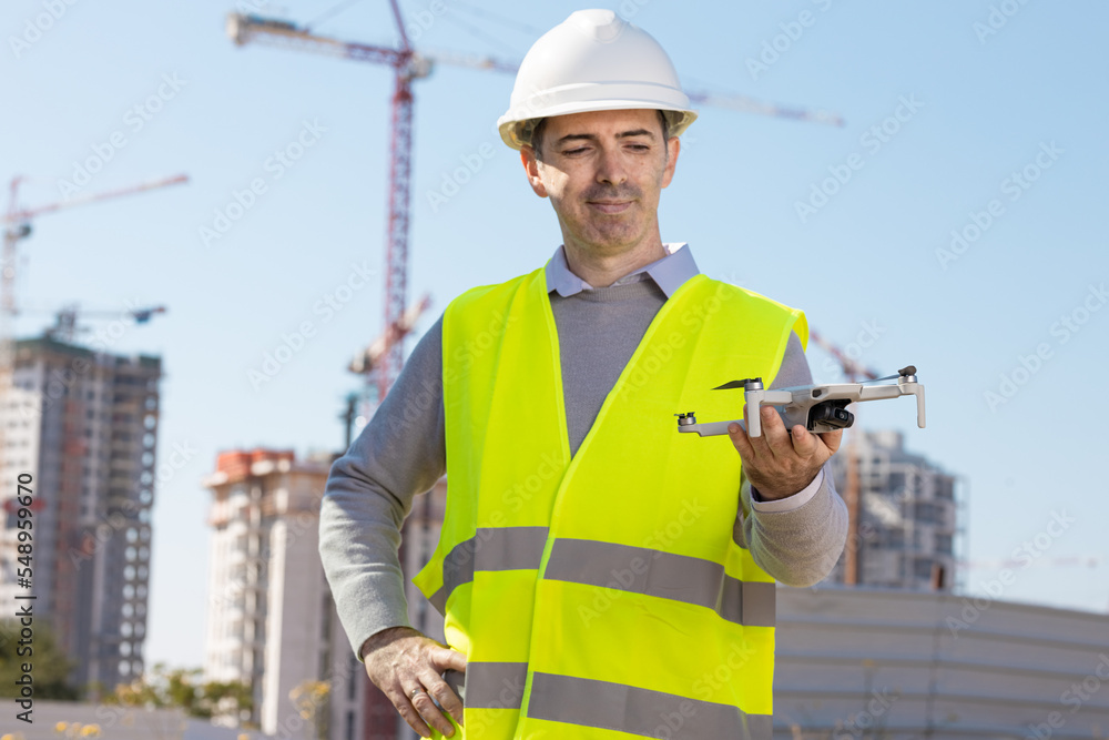 Man launches a quadcopter. An engineer flies a drone next to a construction site. Concept - construction observation with a drone.  Construction cranes on sunset sky