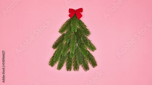 Fir branches making Christmas tree shape with bow on the top on pink background. Flat lay. Stop motion