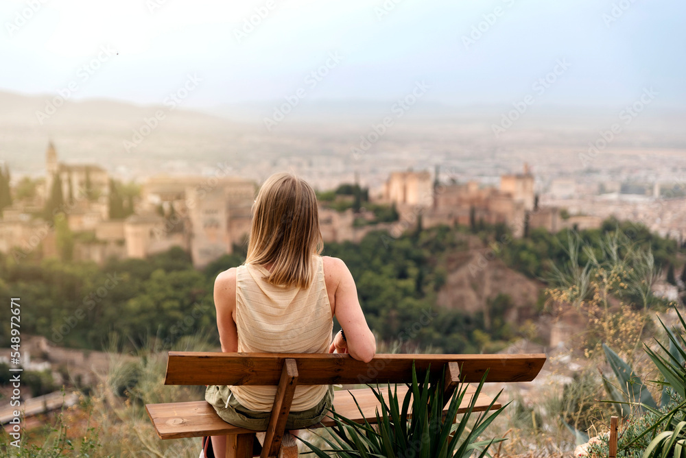 back view of a woman seated in a viewpoint of Granada contemplating views. Visiting Europe back view of a woman seated in a viewpoint of Granada contemplating views. Visiting Europe