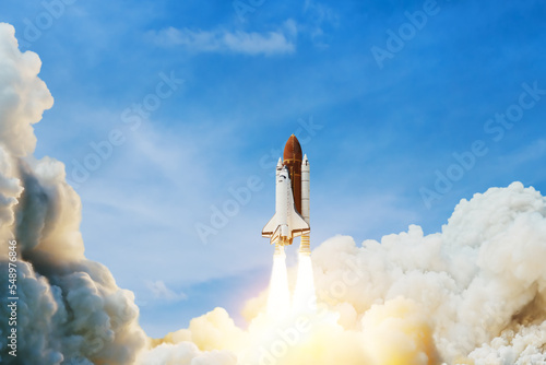 Fototapeta Naklejka Na Ścianę i Meble -  Spaceship lift off. Space shuttle with smoke and blast takes off into space on a background of blue sky. Successful start of a space mission. Elements of this image furnished by NASA.