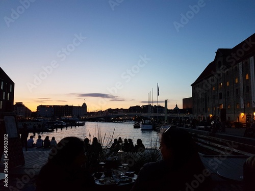 Sun setting behind the canal in the Copenhagen harbour while people are dining.
