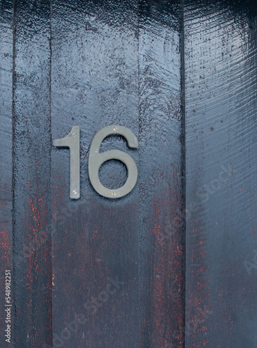 House number 16 (sixteen) in weathered metal on a dark-painted wood facade