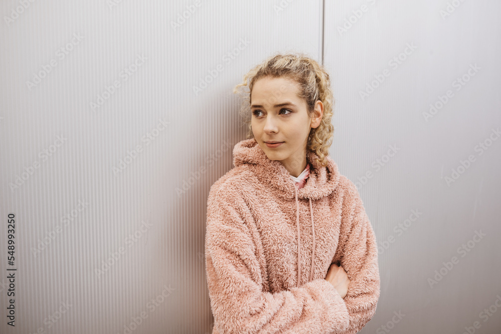 Young blonde serious girl with folded arms stands in front of metal wall and looks to the side Young blonde serious girl with folded arms stands in front of metal wall and looks to the side