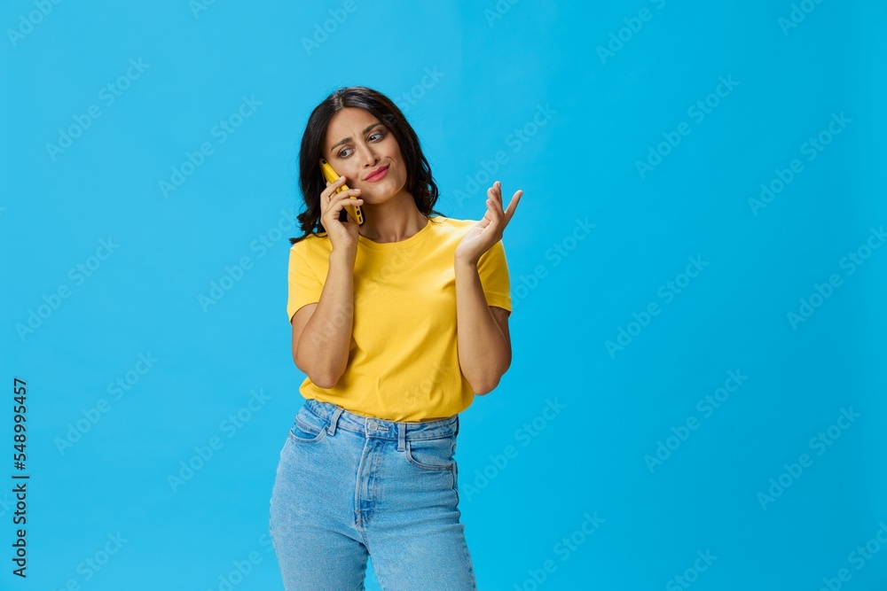 Woman with a phone in her hands with a yellow case on a blue background in a yellow T-shirt, emotions signals gestures, online lifestyle concept, shopping, communication, learning, business online Woman with a phone in her hands with a yellow case on a blue background in a yellow T-shirt, emotions signals gestures, online lifestyle concept, shopping, communication, learning, business online