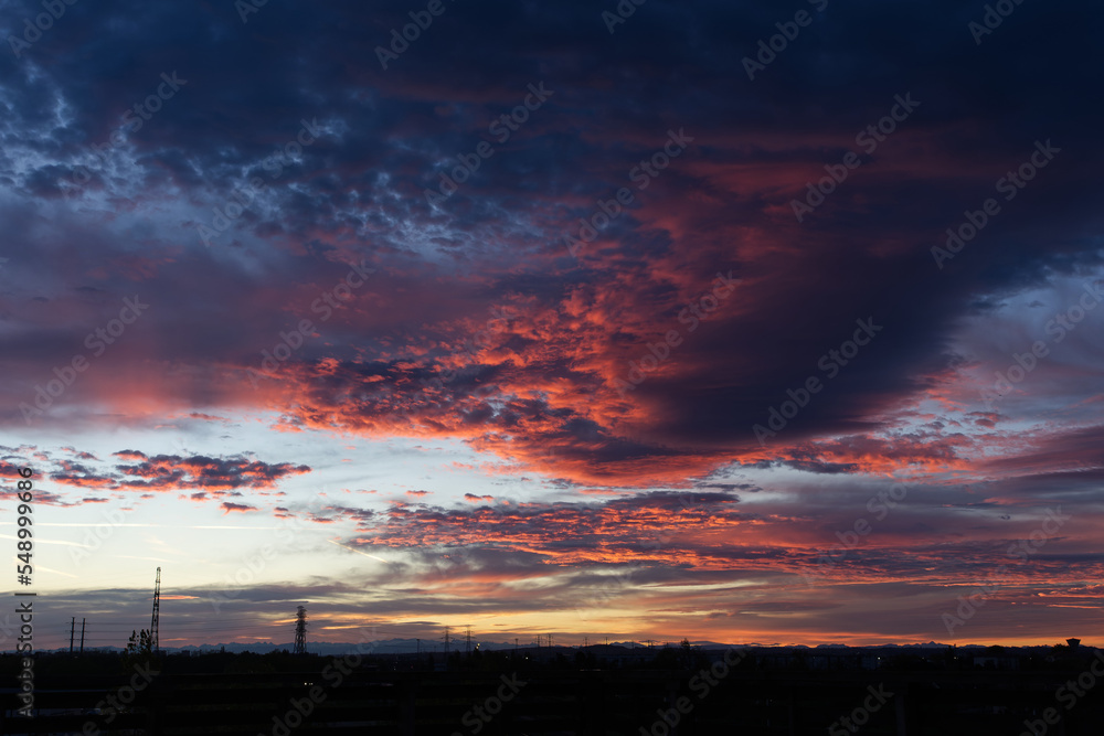 Fototapeta premium Colorful sunrise with heavy clouds with small power lines silhouettes on the horizon
