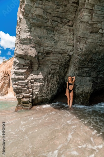 Woman swimsuit sea. Attractive blonde woman in a black swimsuit enjoying the sea air on the seashore around the rocks. Travel and vacation concept.