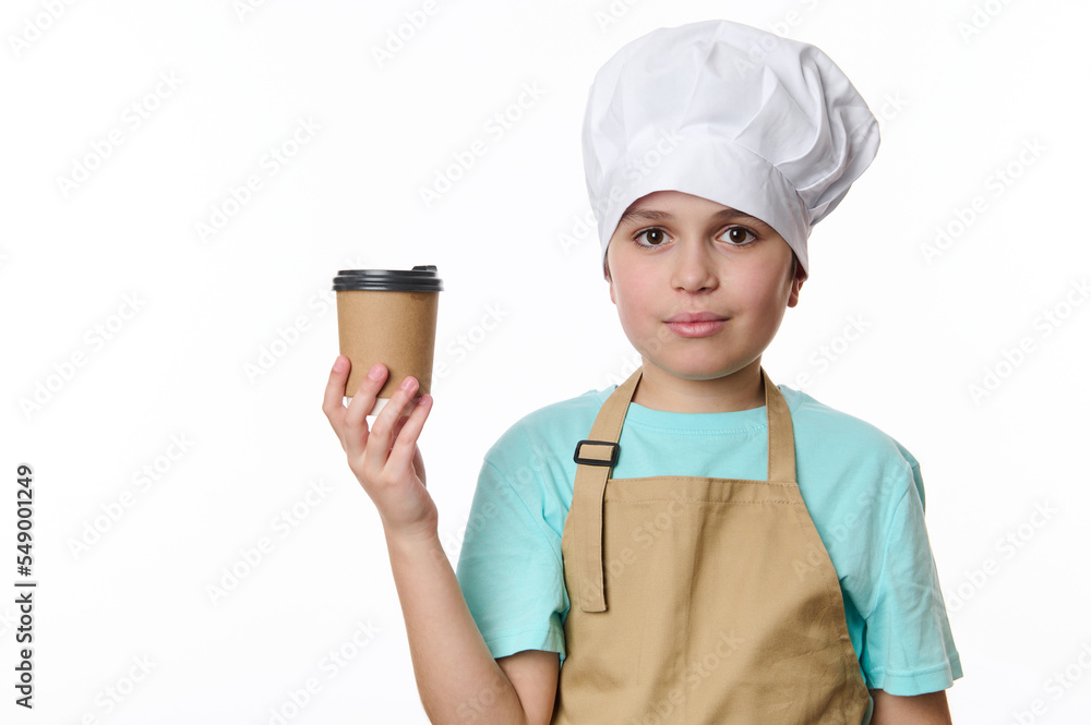 Adorable multi-ethnic teenage boy - barista barman bartender wearing white chef's hat and beige apron, looking at camera while holding a takeaway hot drink in cardboard cup to go, isolated on white Adorable multi-ethnic teenage boy - barista barman bartender wearing white chef's hat and beige apron, looking at camera while holding a takeaway hot drink in cardboard cup to go, isolated on white