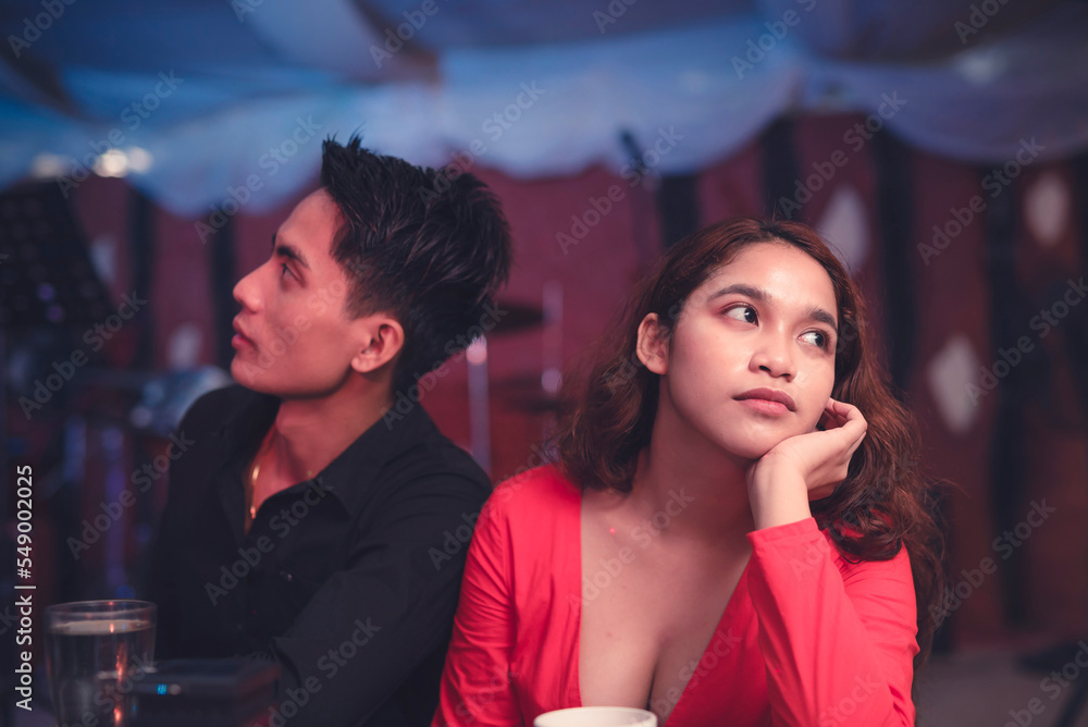 A couple having a date at an elegant restaurant sits back to back and ignores each other as they are having an argument. A lady is upset with her insensitive boyfriend. Waiting for the night to end.
