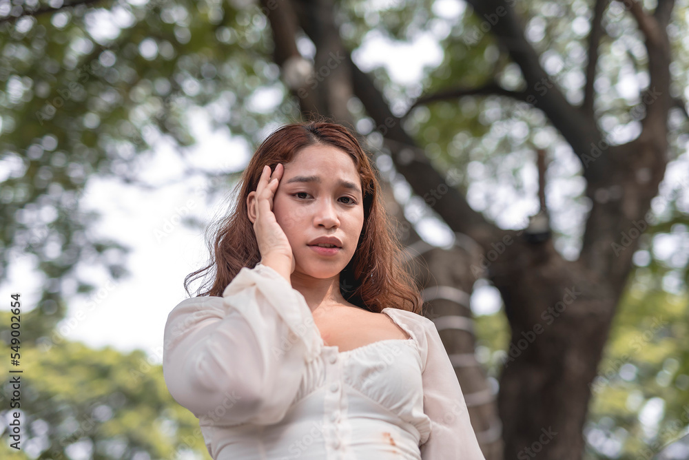 A Southeast Asian lady massages the temple of her forehead with a worried look on her face.