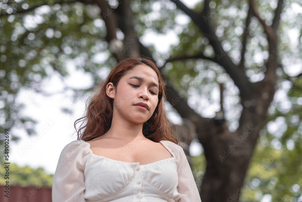 A low-angle shot of a woman looking down with an upset facial expression. Taken with a trees background. A low-angle shot of a woman looking down with an upset facial expression. Taken with a trees background.