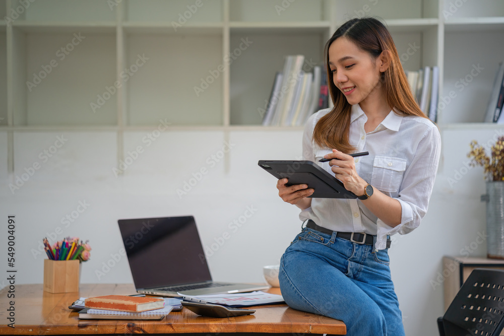 Asian businesswoman sitting on an office desk and using a tablet. Asian businesswoman sitting on an office desk and using a tablet.