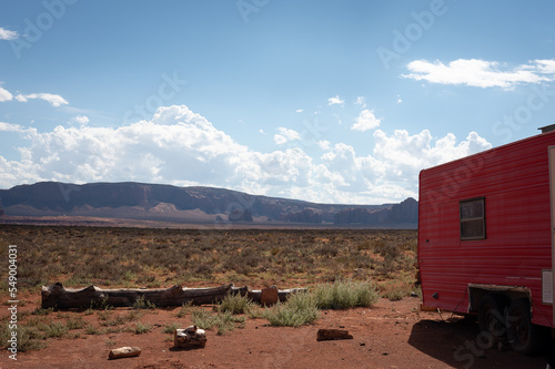 An old red camper trailer and logs for sitting in the desert of Monument Valley