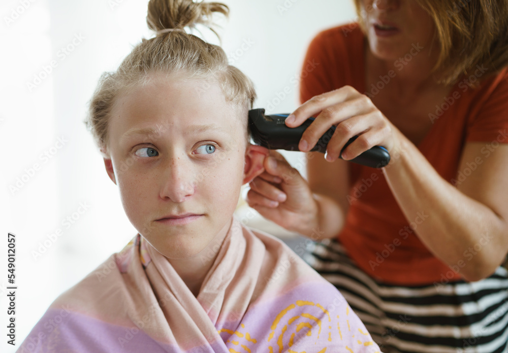 Fototapeta premium Mother trimming her son hairs making a modern hairstyle using electric electric trimmer at their home living room.
