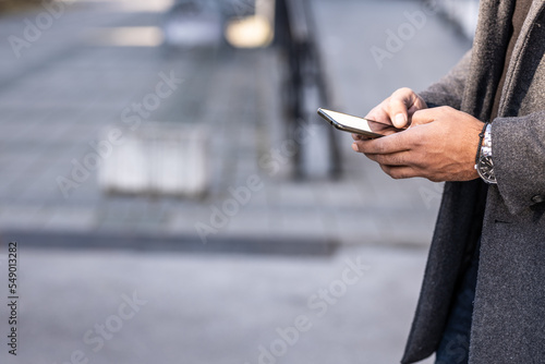 Close up of business man hands using modern technology, mobile phone and laptop outdoors