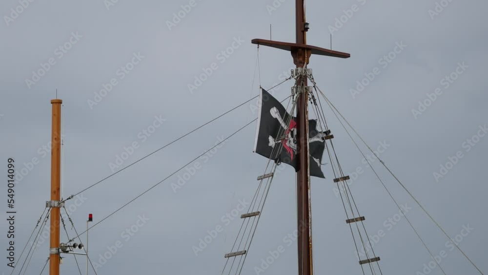 Ship with black pirate flag on mast. Black flag with skull and crossbones swings in wind. Jolly roger flutters on yardarm against gray overcast sky. Rovinj, Istria, Croatia - November 19, 2022 Ship with black pirate flag on mast. Black flag with skull and crossbones swings in wind. Jolly roger flutters on yardarm against gray overcast sky. Rovinj, Istria, Croatia - November 19, 2022