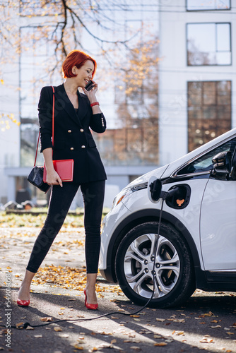 Business woman with notebook standing by electric car charging © Petro