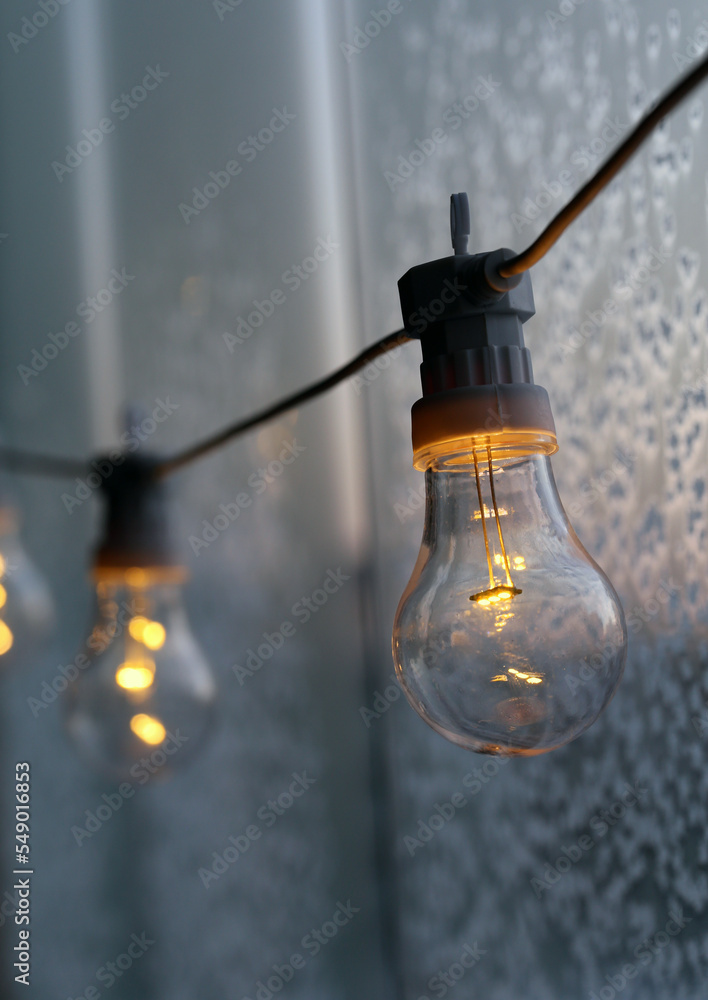 Decorative simple light bulb hanging on a balcony during a cold day. Glass with ice crystals in the background. Energy, energy crisis, electricity and wintertime concept. Winter wonderland Finland.