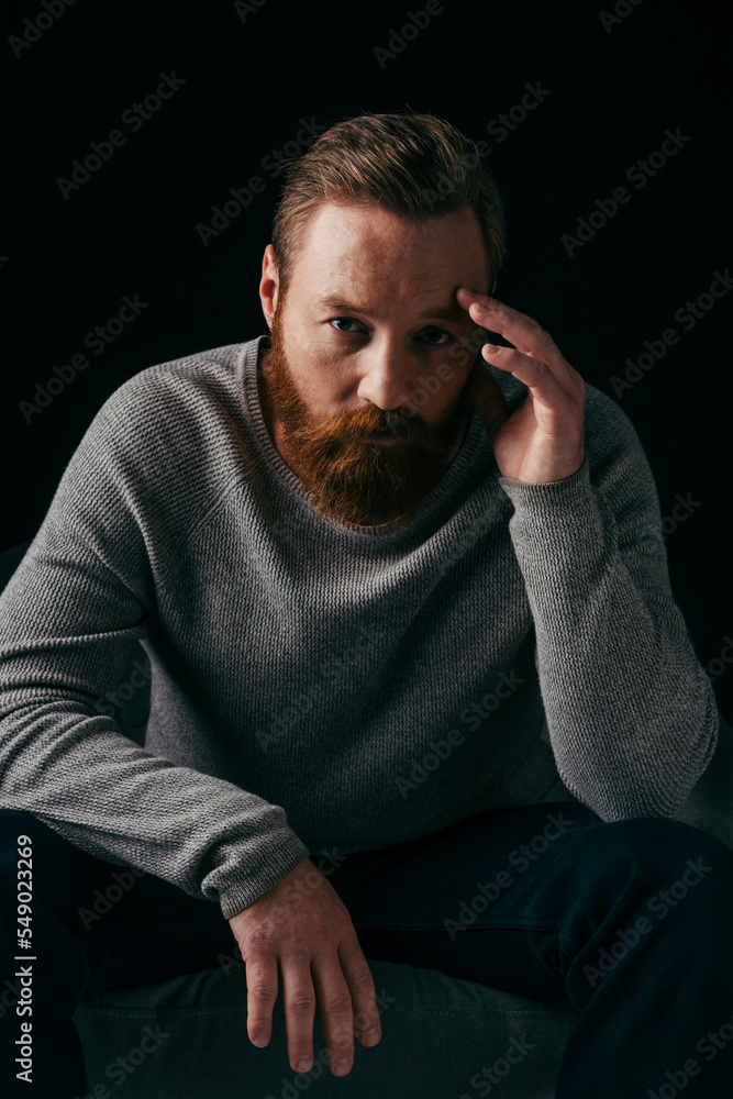 Portrait of bearded man looking at camera near armchair isolated on black. Portrait of bearded man looking at camera near armchair isolated on black.