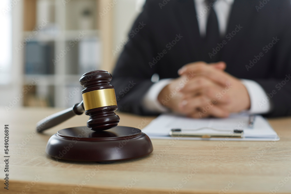 Close up brown wooden gavel on sound block placed on table of professional lawyer or attorney. Closeup judge's hammer on desk, with law expert in background. Legal services, law consultation concept